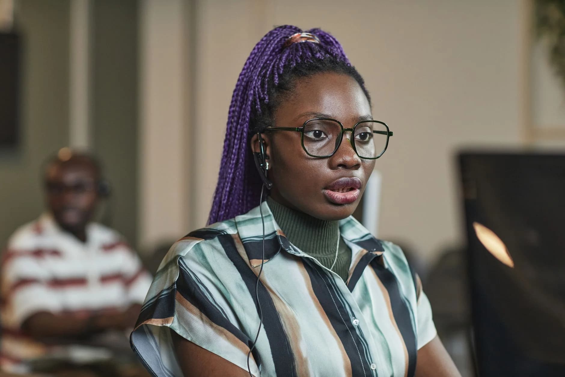 Close portrait of a woman wearing eyeglasses and a headset, focused on listening