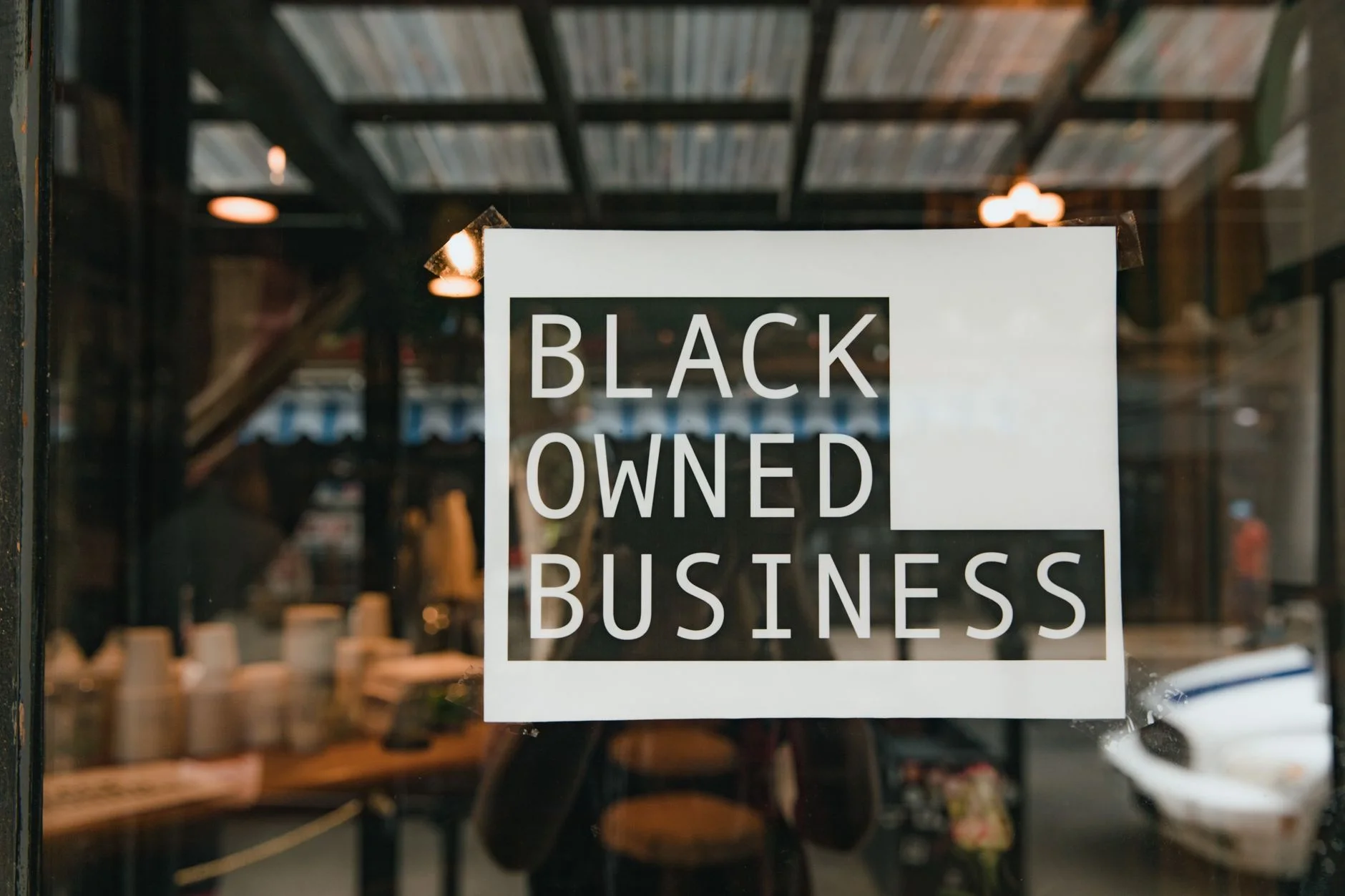 Store window with black owned business sign taped on a window, seen from outside a store.