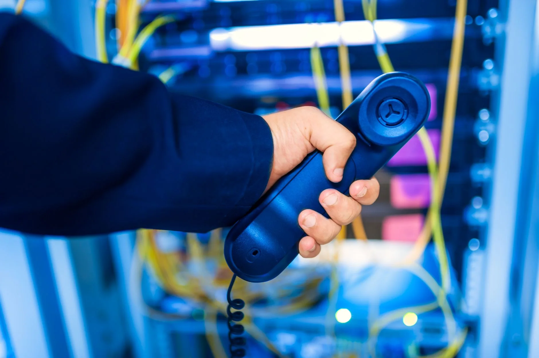 Hand holding telephone receiver with rack and wiring in background